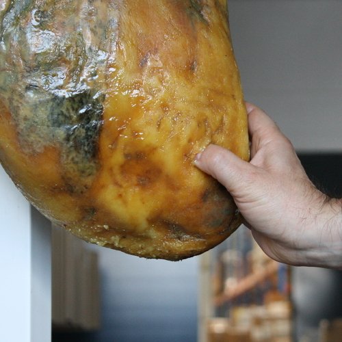 Primo piano del pollice che affonda nel grasso di un prosciutto iberico